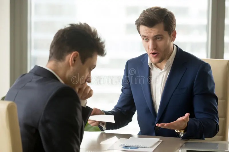 Manager scolding a deflated employee across a desk