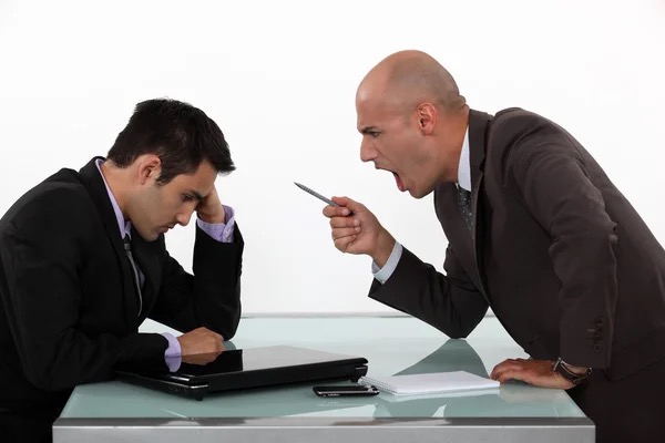 Boss shouting at a hunched employee across a desk